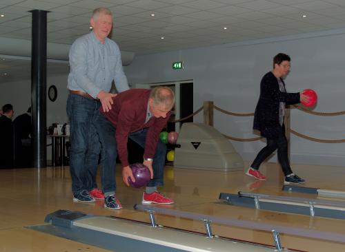 Herman helpt Wim zodat hij een goede score kan halen tijdens de bowlingmiddag. Op de achtergrond staat Marina klaar voor haar beurt